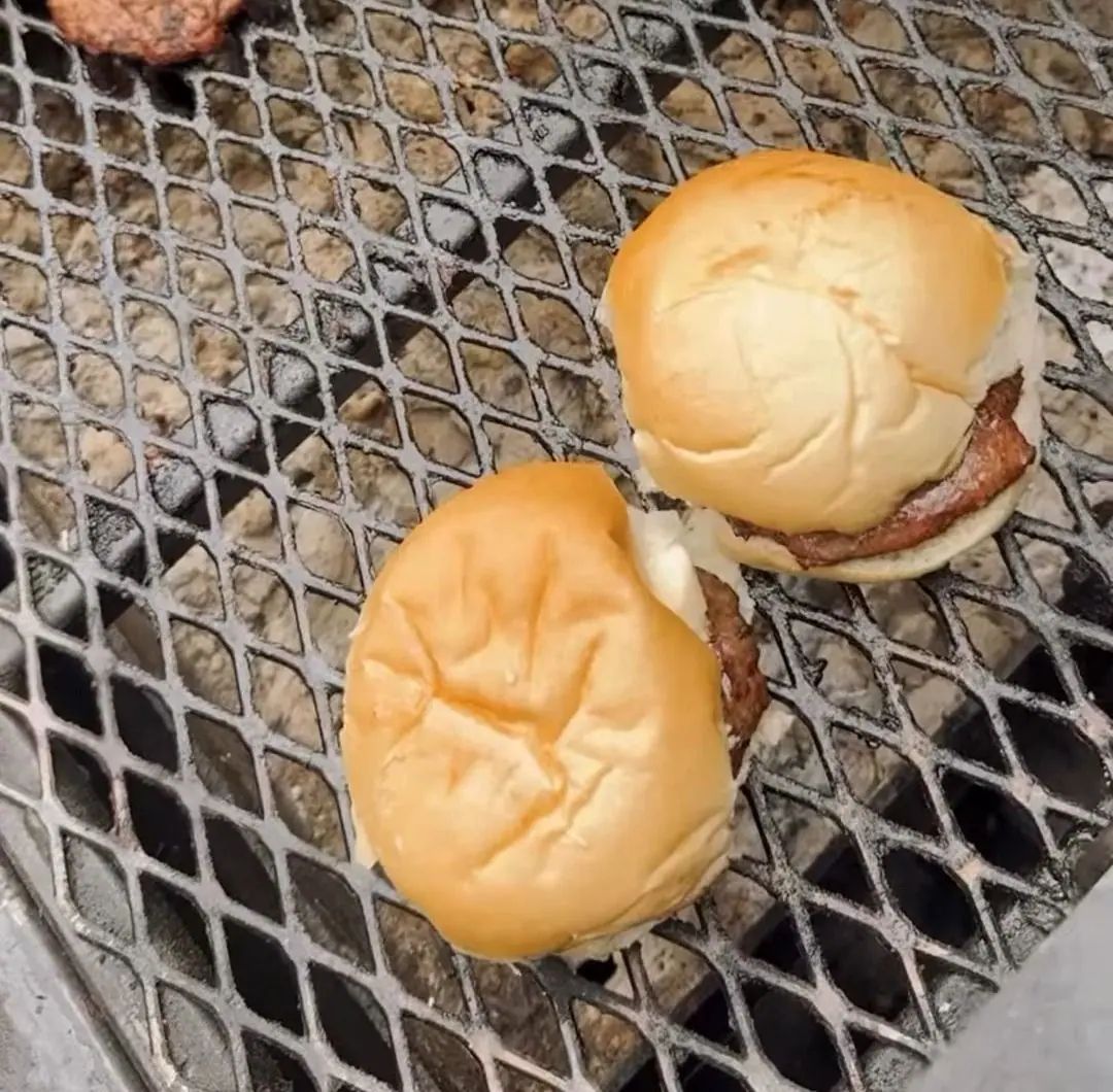 Two burgers in soft buns and a patty on the grill grate