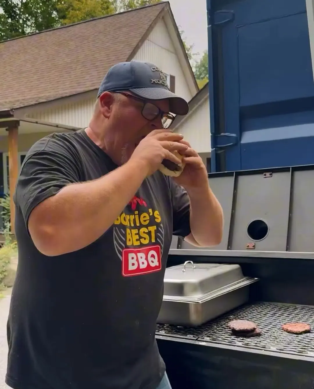 Aaron taking a bite of a burger beside the grill at a backyard party